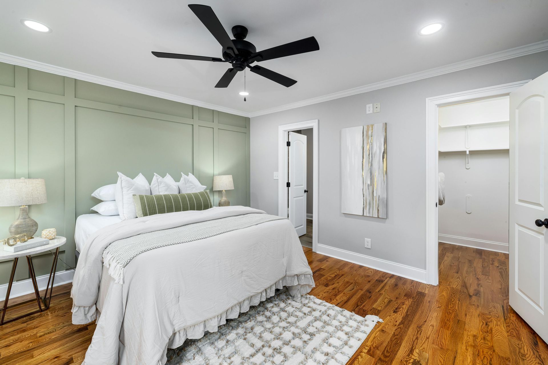 A bedroom with a bed , ceiling fan , and hardwood floors.