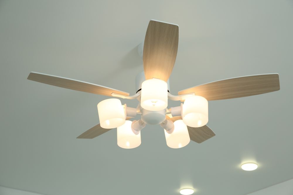 Ceiling fan with wooden blades and four lit frosted glass lights in a white room
