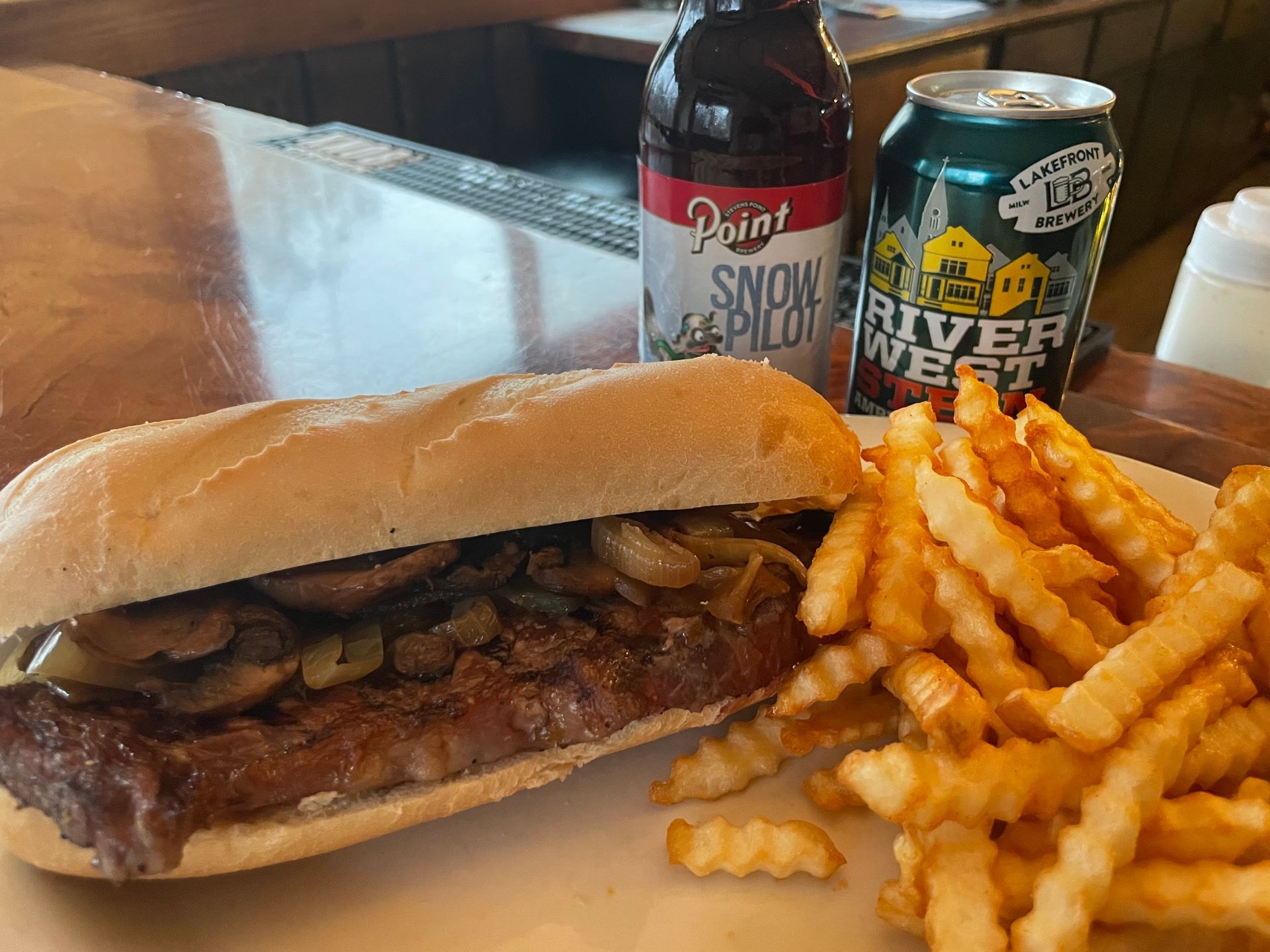 A sandwich and french fries are on a plate next to a can of river west beer.