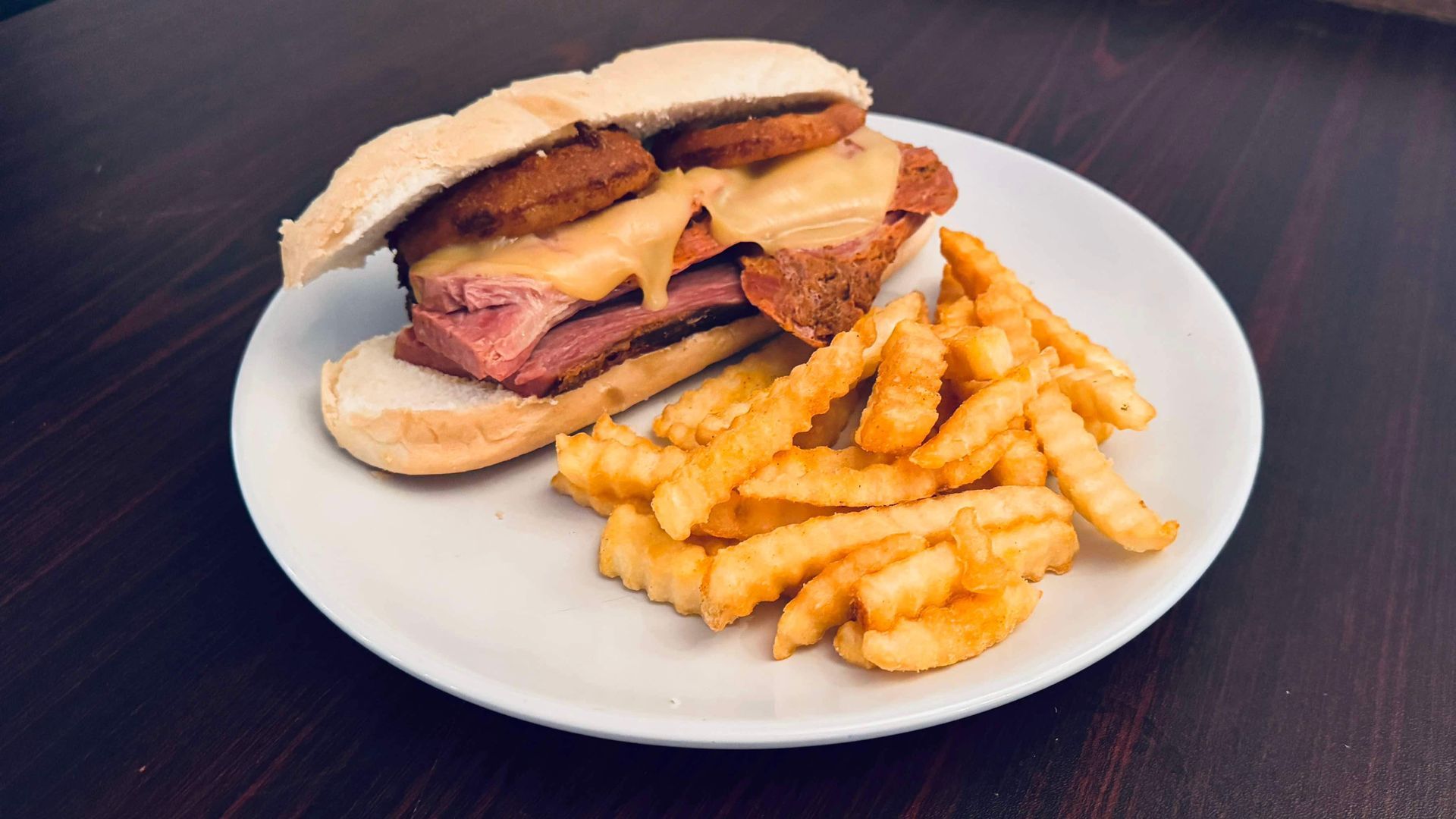 A sandwich and french fries on a white plate on a table.