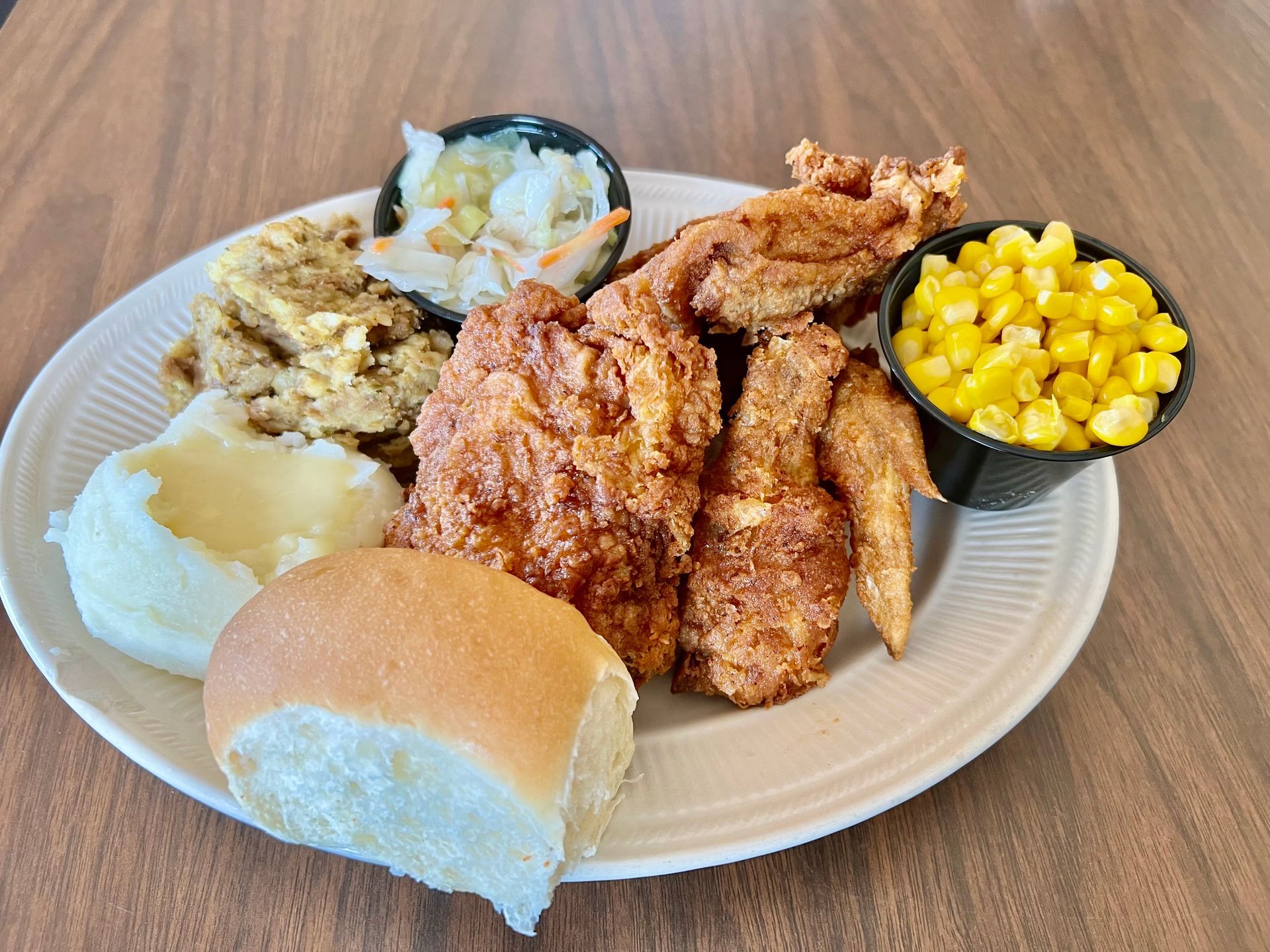 A white plate topped with fried chicken , mashed potatoes , corn and a roll.