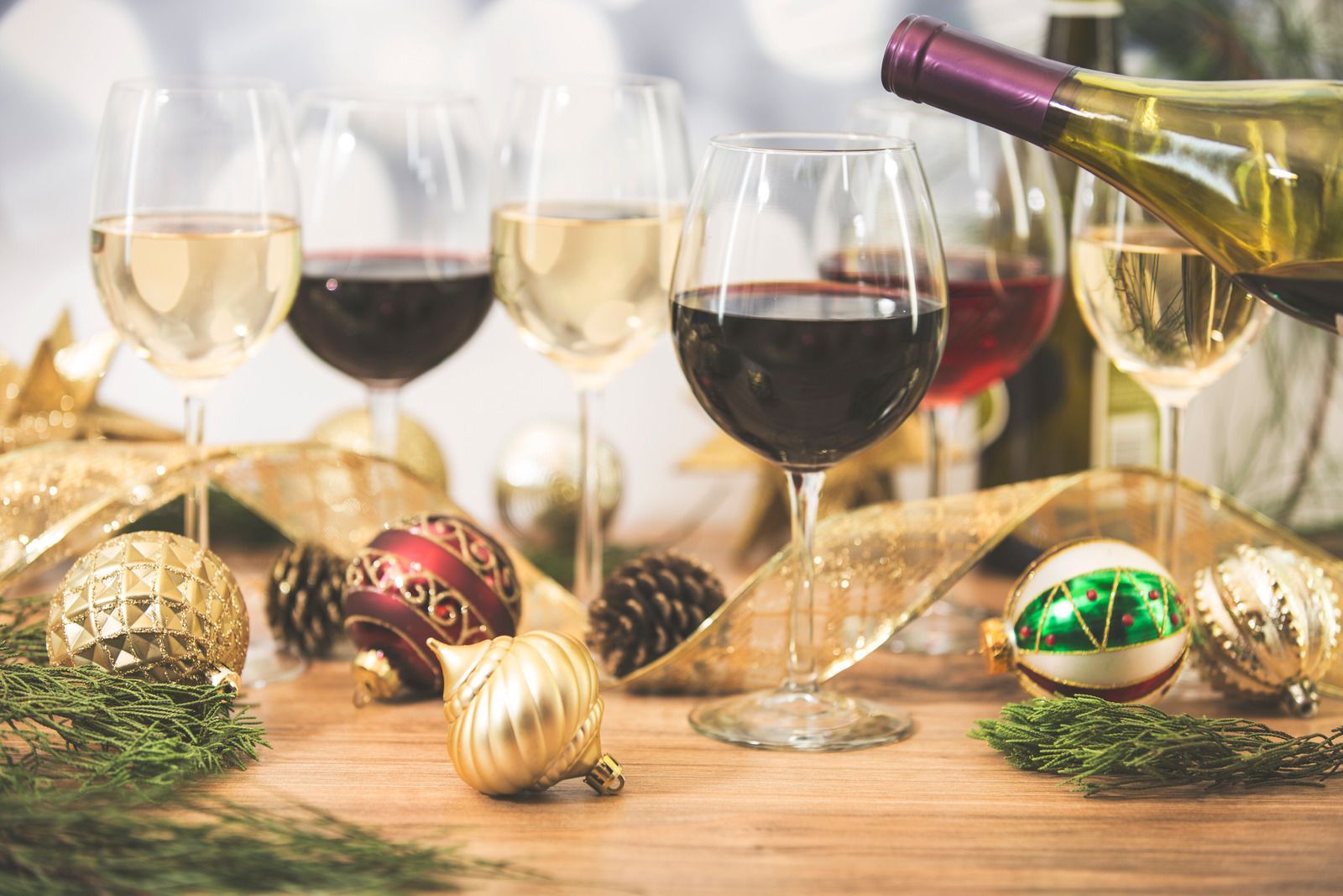 Wine glasses and a bottle on a festive table with gold ornaments and pine sprigs