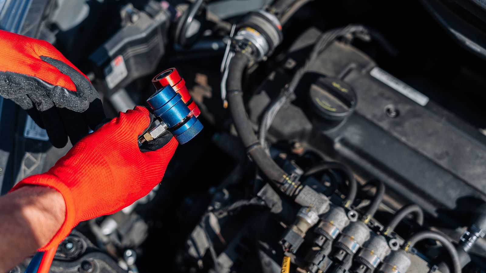 A person wearing red gloves is working on a car engine.