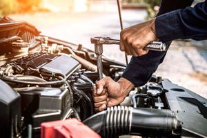 A man is working on the engine of a car with a wrench.