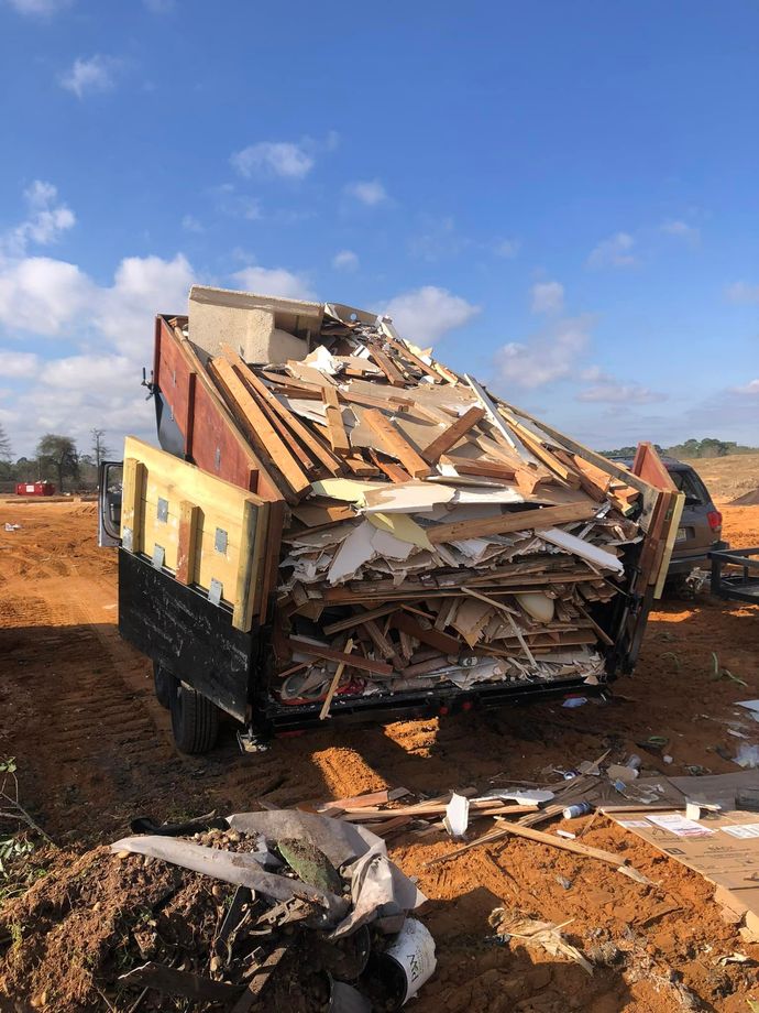 Damaged truck dump body with crushed debris on a dirt lot under a blue sky