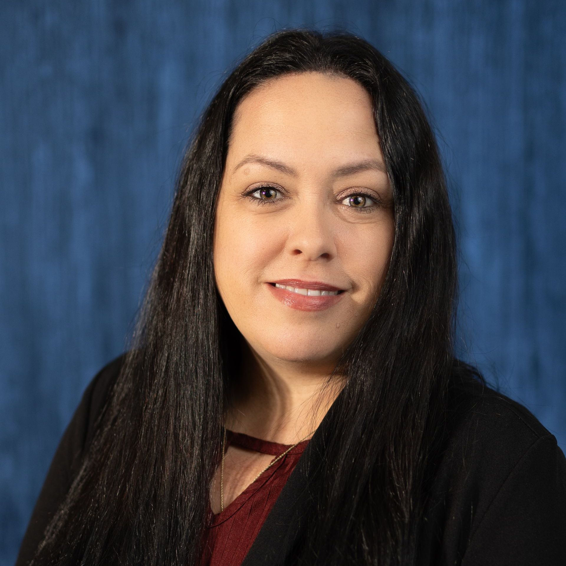A woman with long black hair is smiling for a picture in front of a blue background.