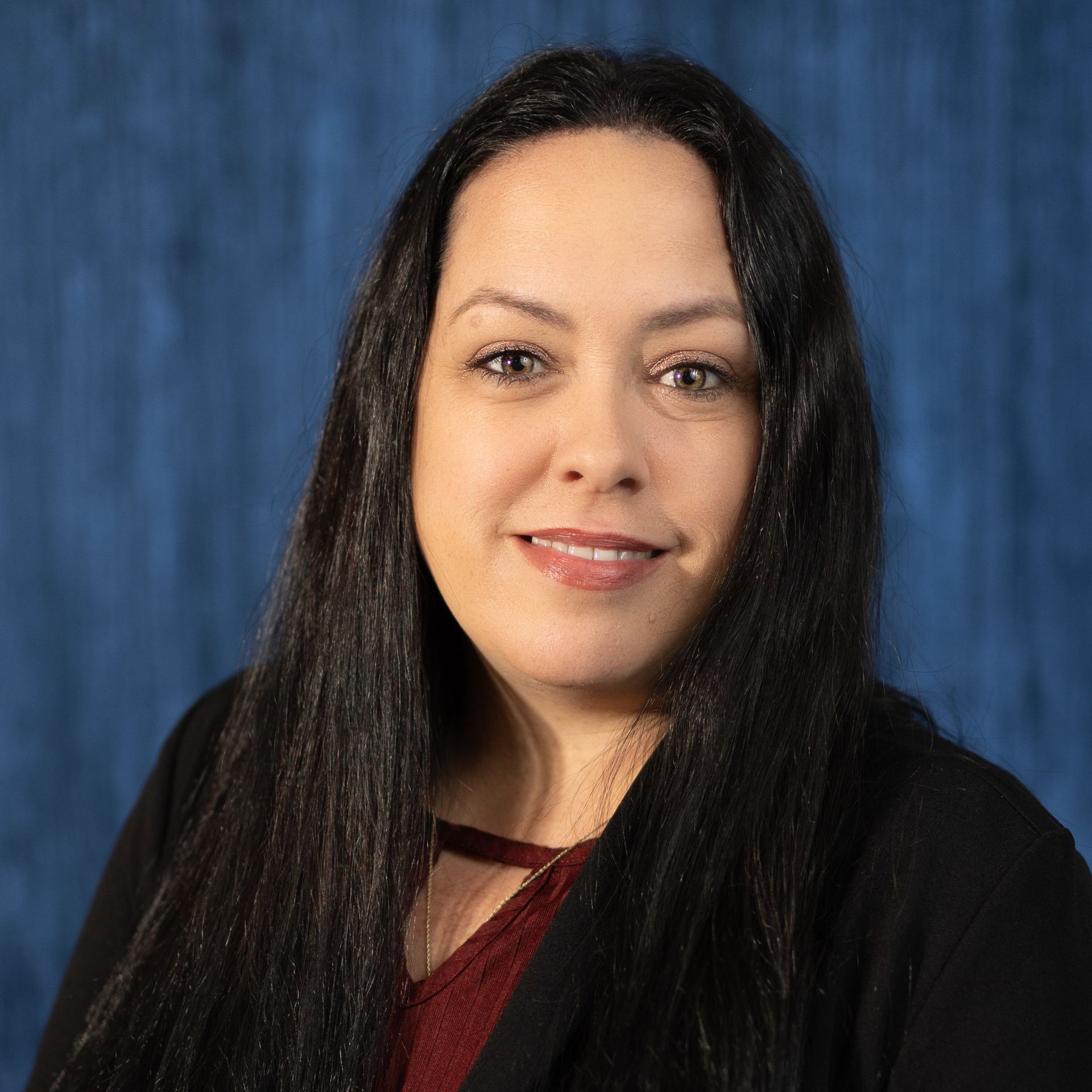 A woman with long black hair is wearing a black jacket and a red shirt.