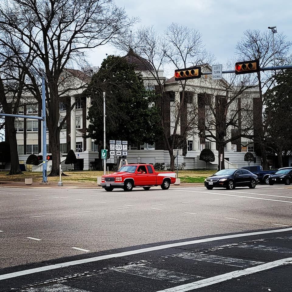 A red truck is driving down a street in front of a large building