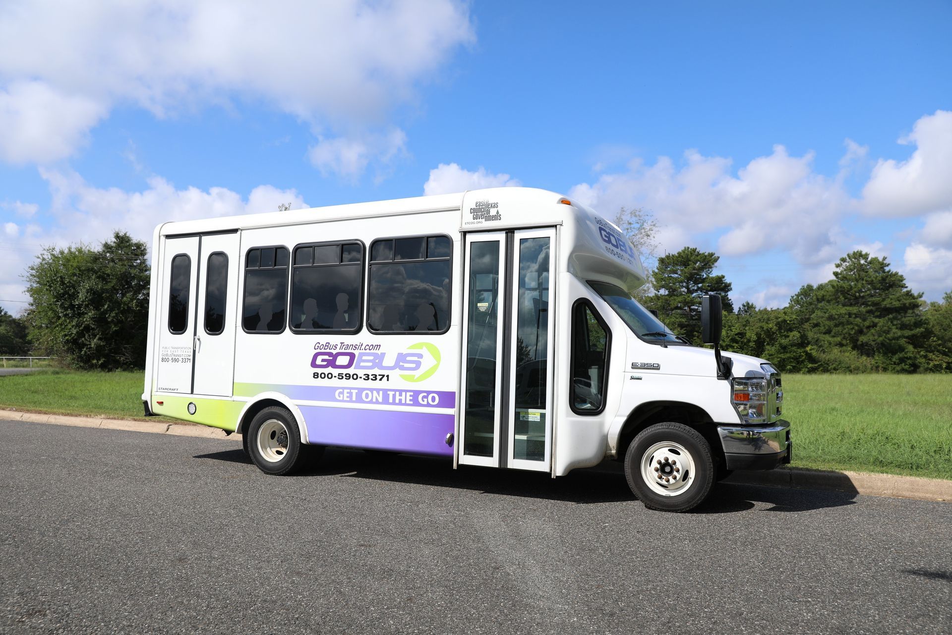 A white and purple bus is parked on the side of the road.