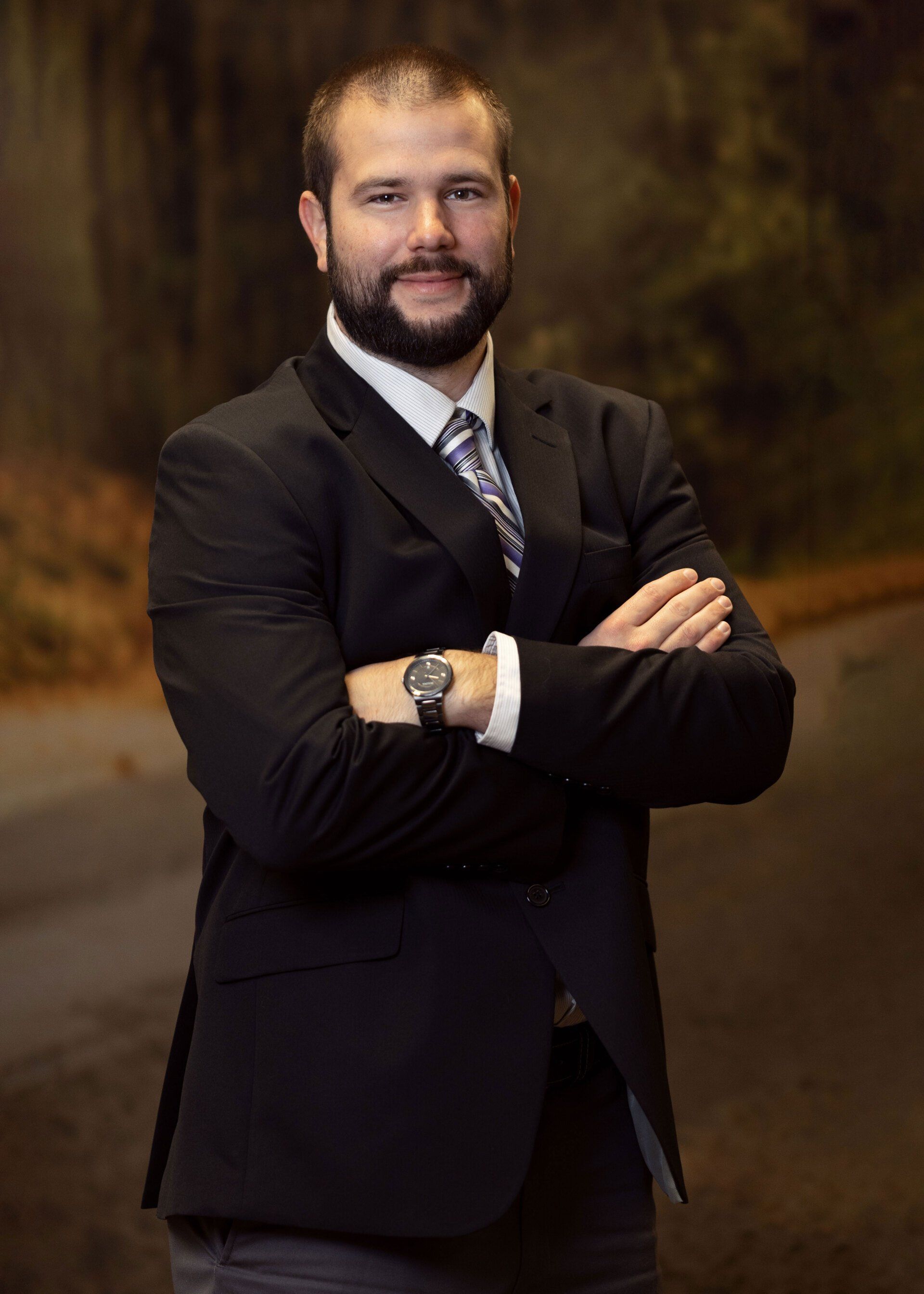 A man in a suit and tie is standing with his arms crossed.