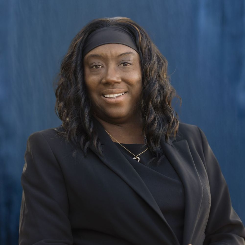 A woman in a black jacket and headband is smiling for the camera.