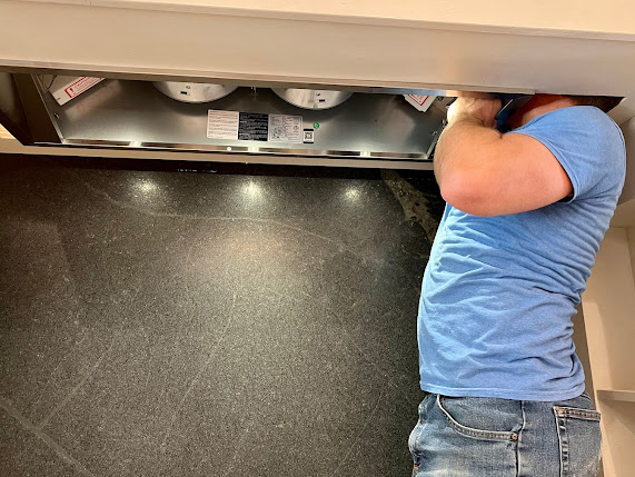 A man in a blue shirt is working on a kitchen hood.