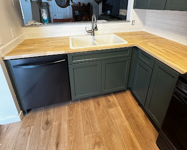 A kitchen with a sink , dishwasher , and wooden counter tops.