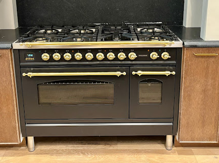 A black stove with gold handles is sitting in a kitchen next to wooden cabinets.