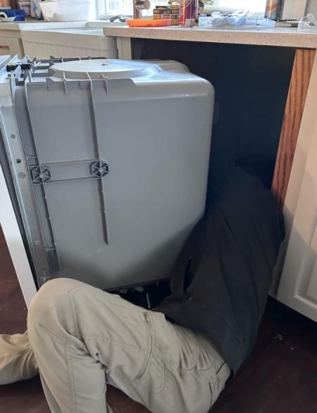 A man is kneeling under a dishwasher in a kitchen.