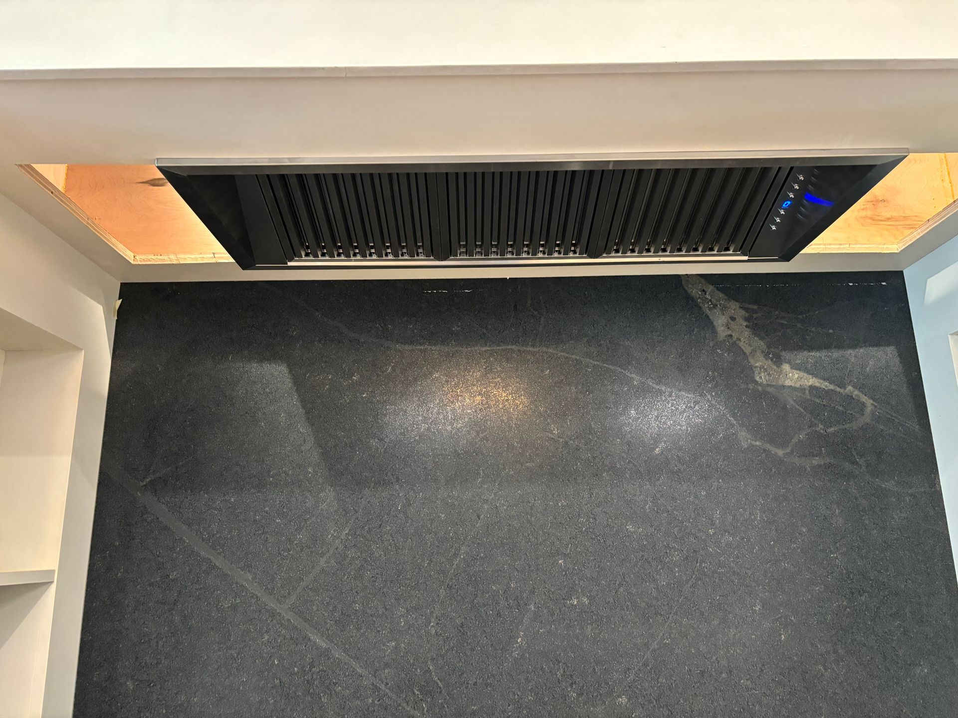 A kitchen with a black counter top and a hood above it.