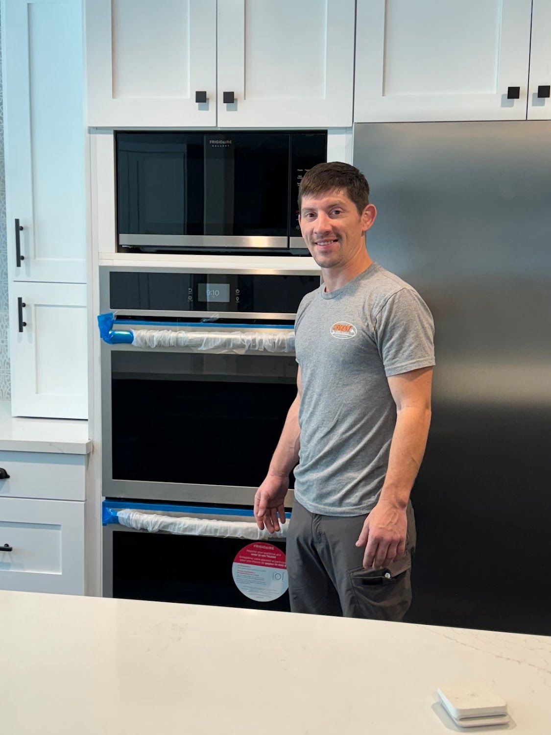 A man is standing in a kitchen next to a refrigerator and oven.