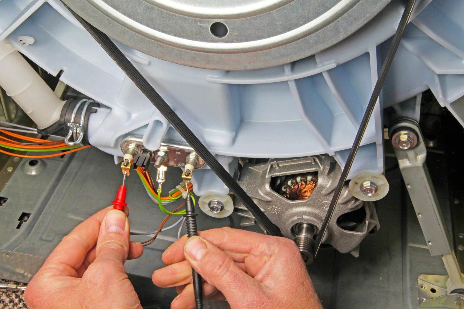 Hands holding multimeter probes, testing electrical connections on a washing machine motor.