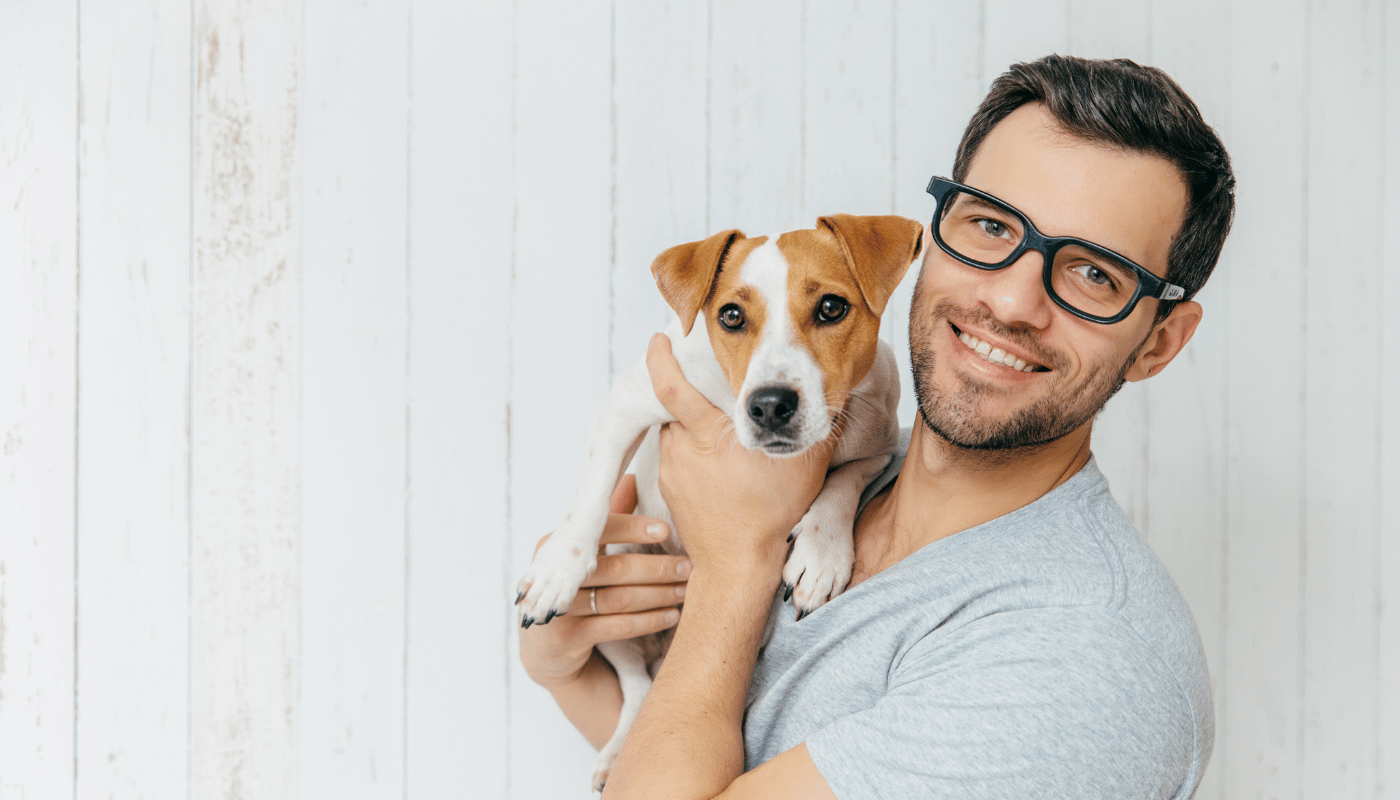 A man wearing glasses is holding a small dog in his arms.