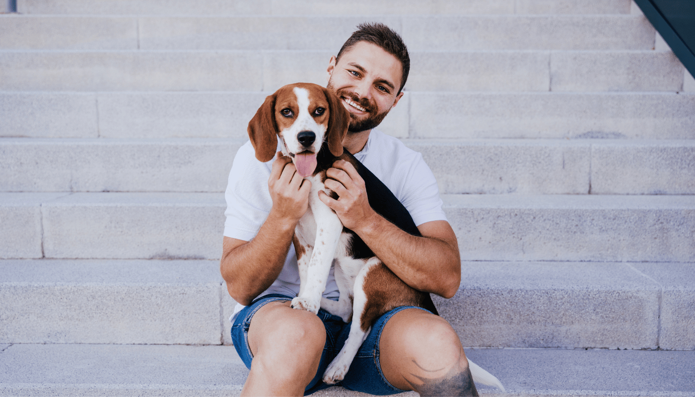 A man is sitting on a set of stairs holding a beagle dog.