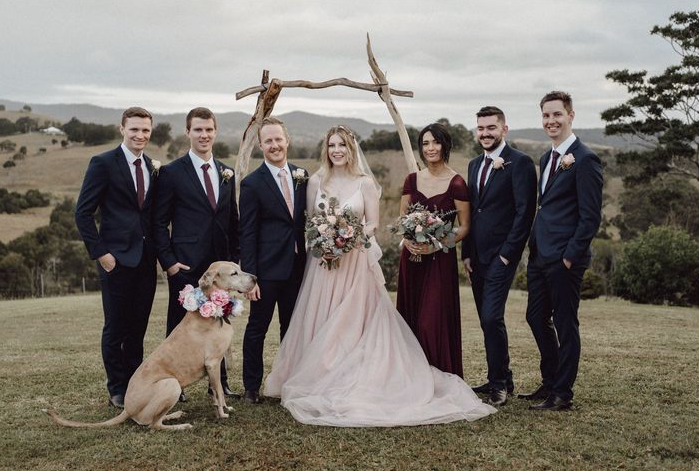 A bride and groom are posing for a picture with their wedding party and a dog.