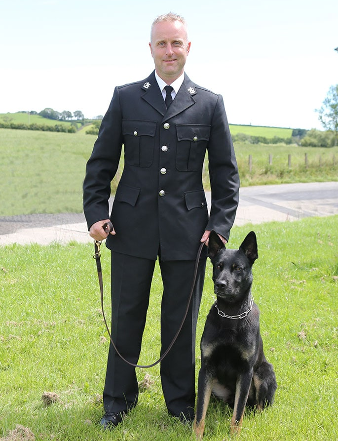 A man in a suit is standing next to a black dog on a leash
