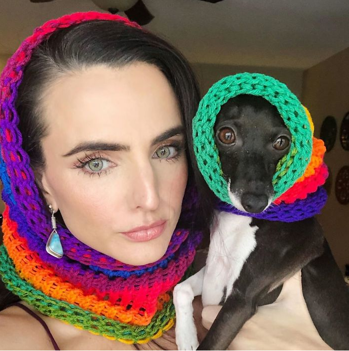 A woman is holding a small black and white dog wearing a colorful scarf