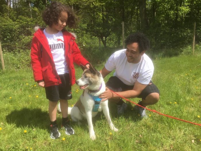 A man and a boy are kneeling down next to a dog on a leash.
