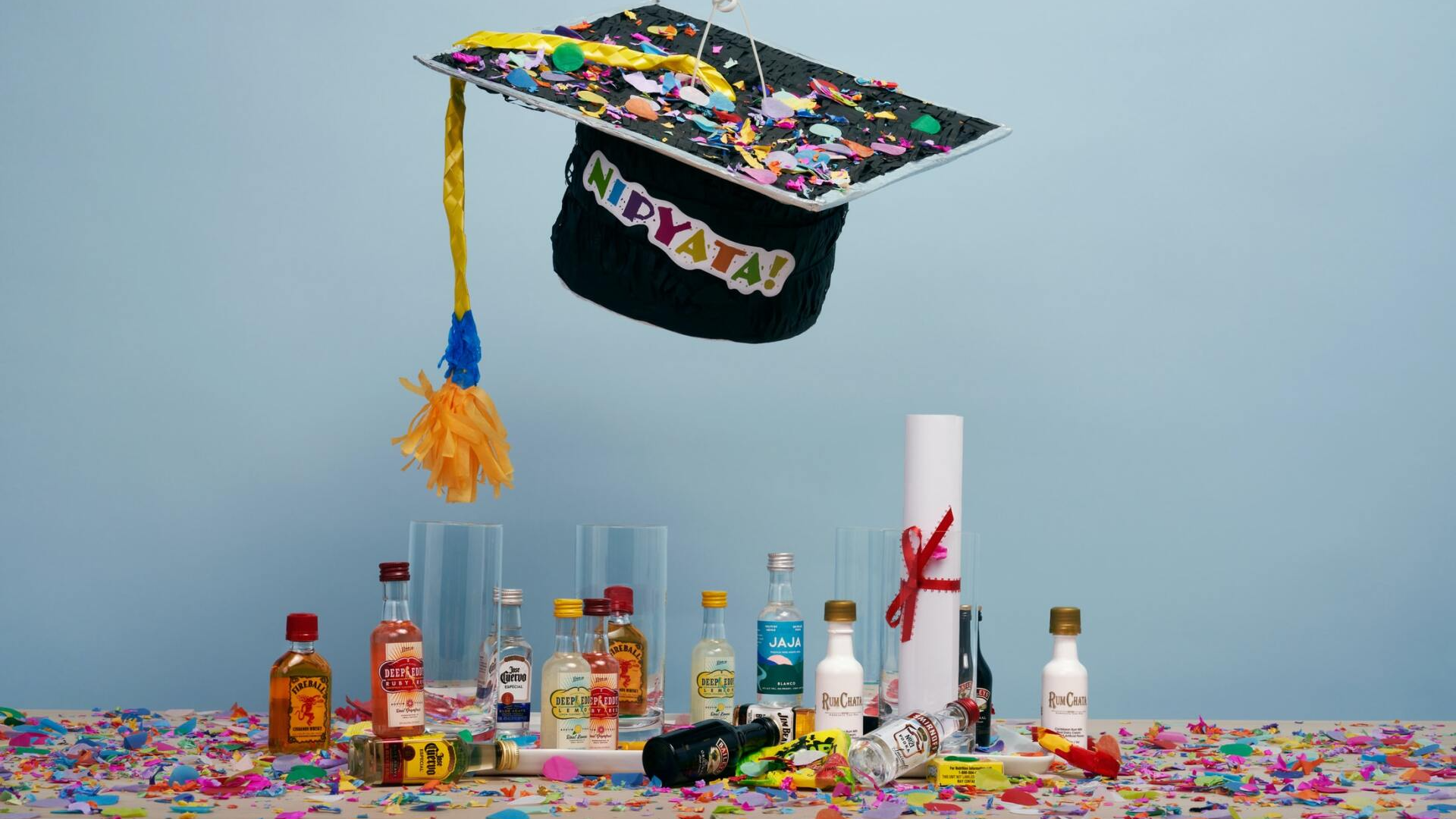 A graduation cap is sitting on top of a table with bottles of alcohol and confetti.