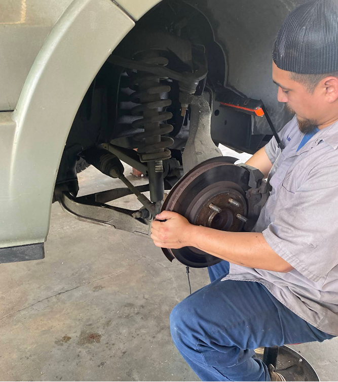 Mechanic working on a vehicle's front suspension and brake rotor in a shop. | Driver's Choice