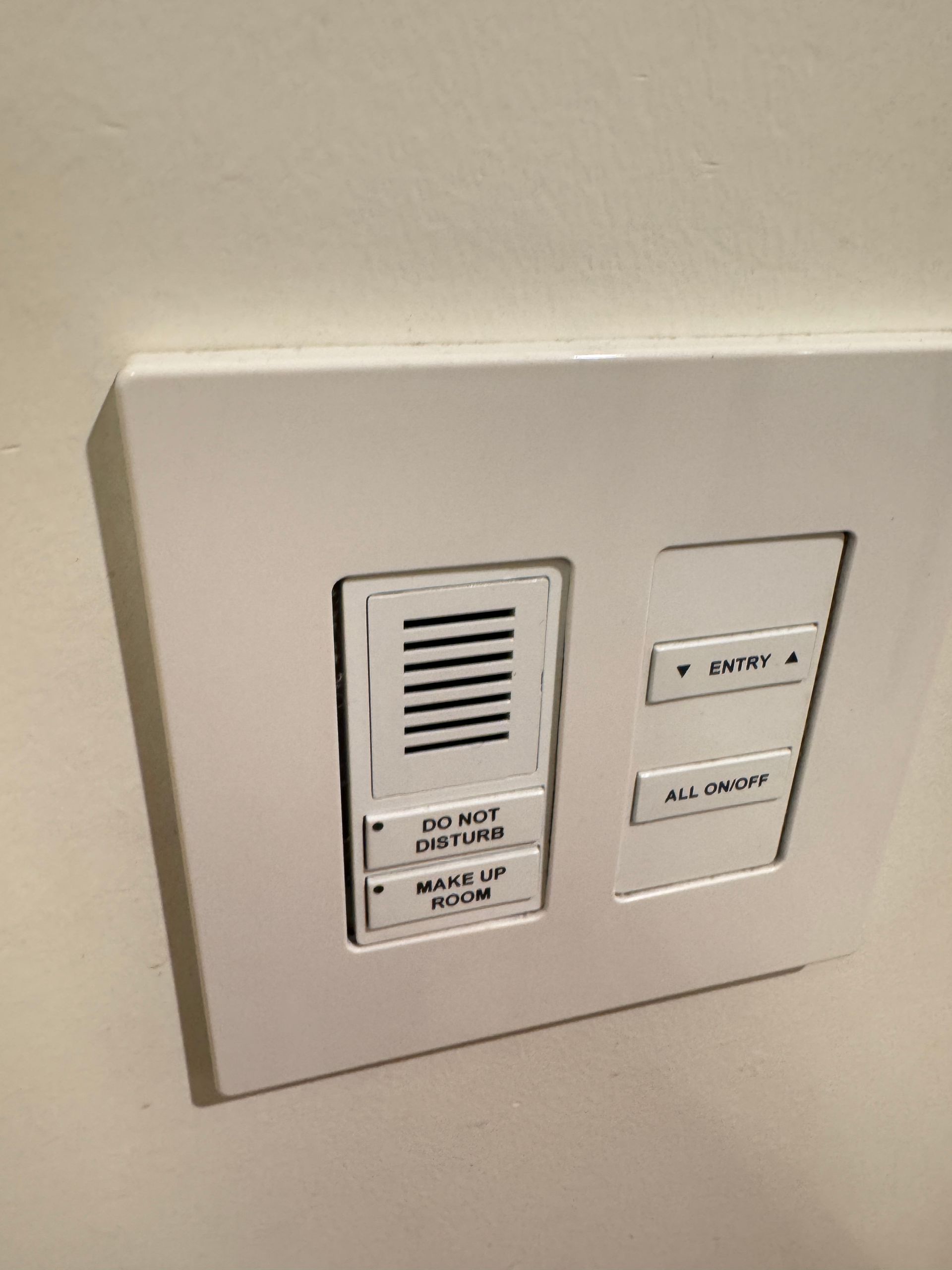 A white, wall-mounted hotel room control panel with buttons for 