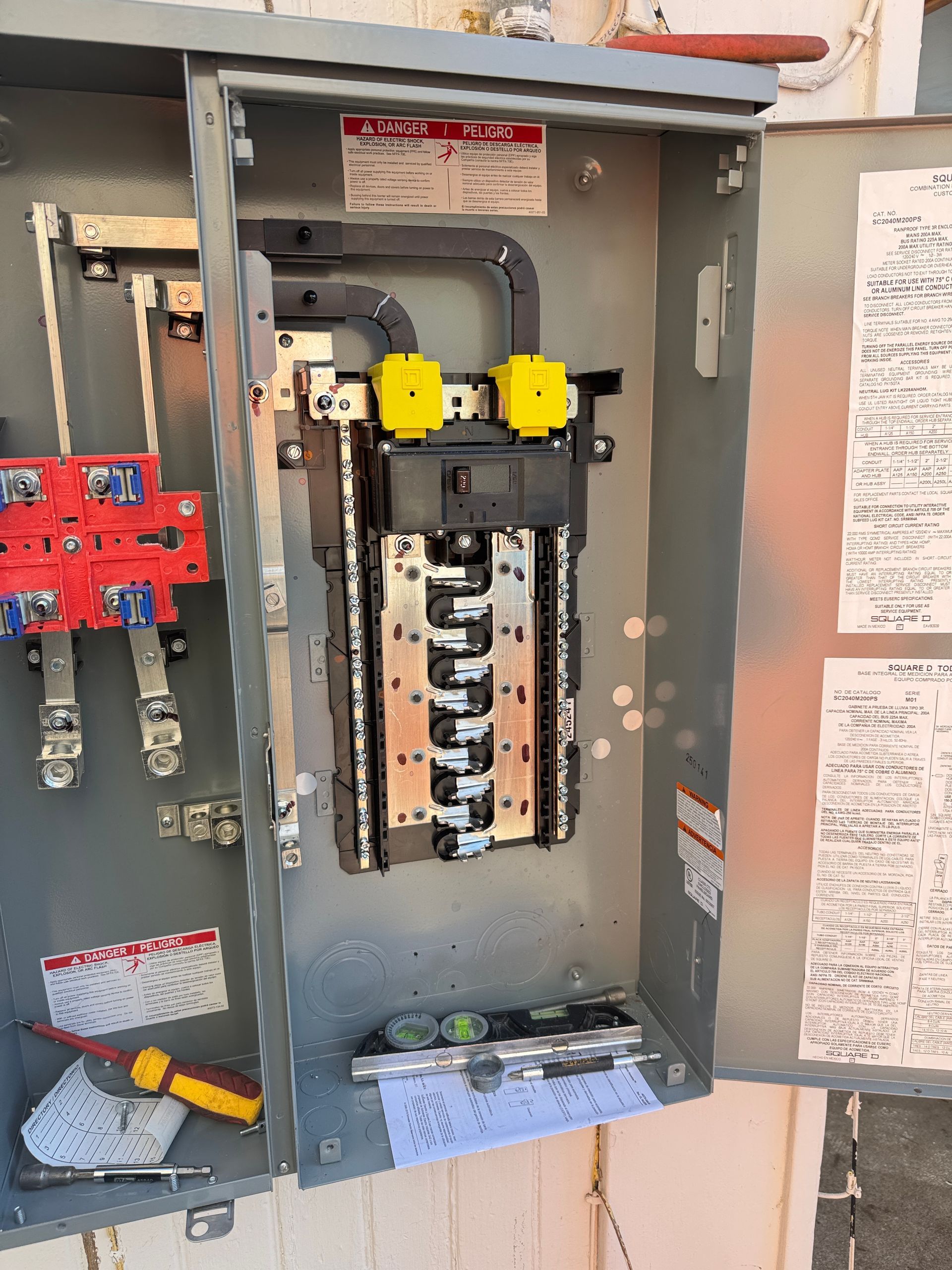 An open electrical panel with a central bus bar, a red terminal block on the left, and tools resting in the bottom.