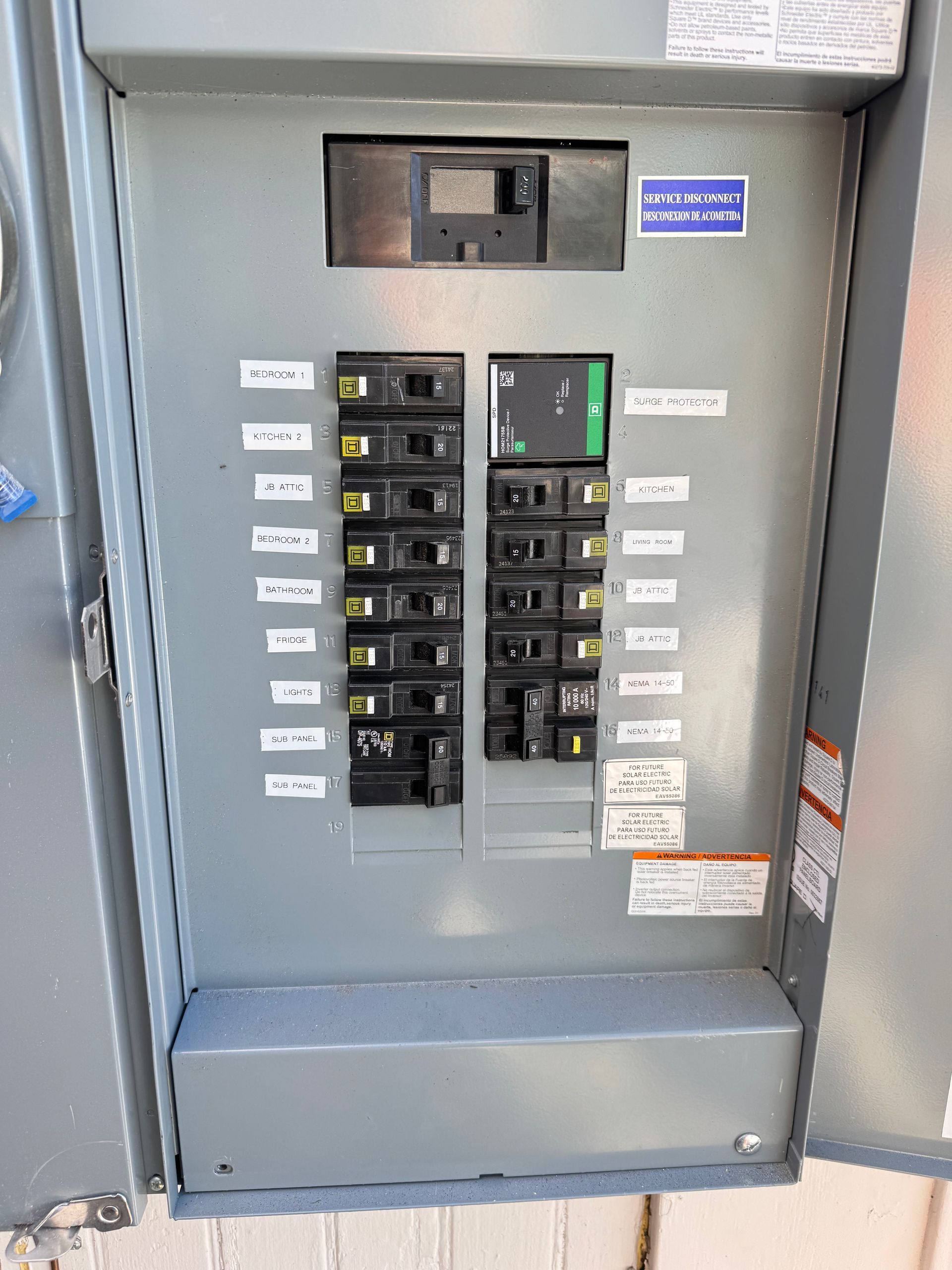 An open electrical breaker panel with various labeled circuit switches mounted on a gray metal backboard.