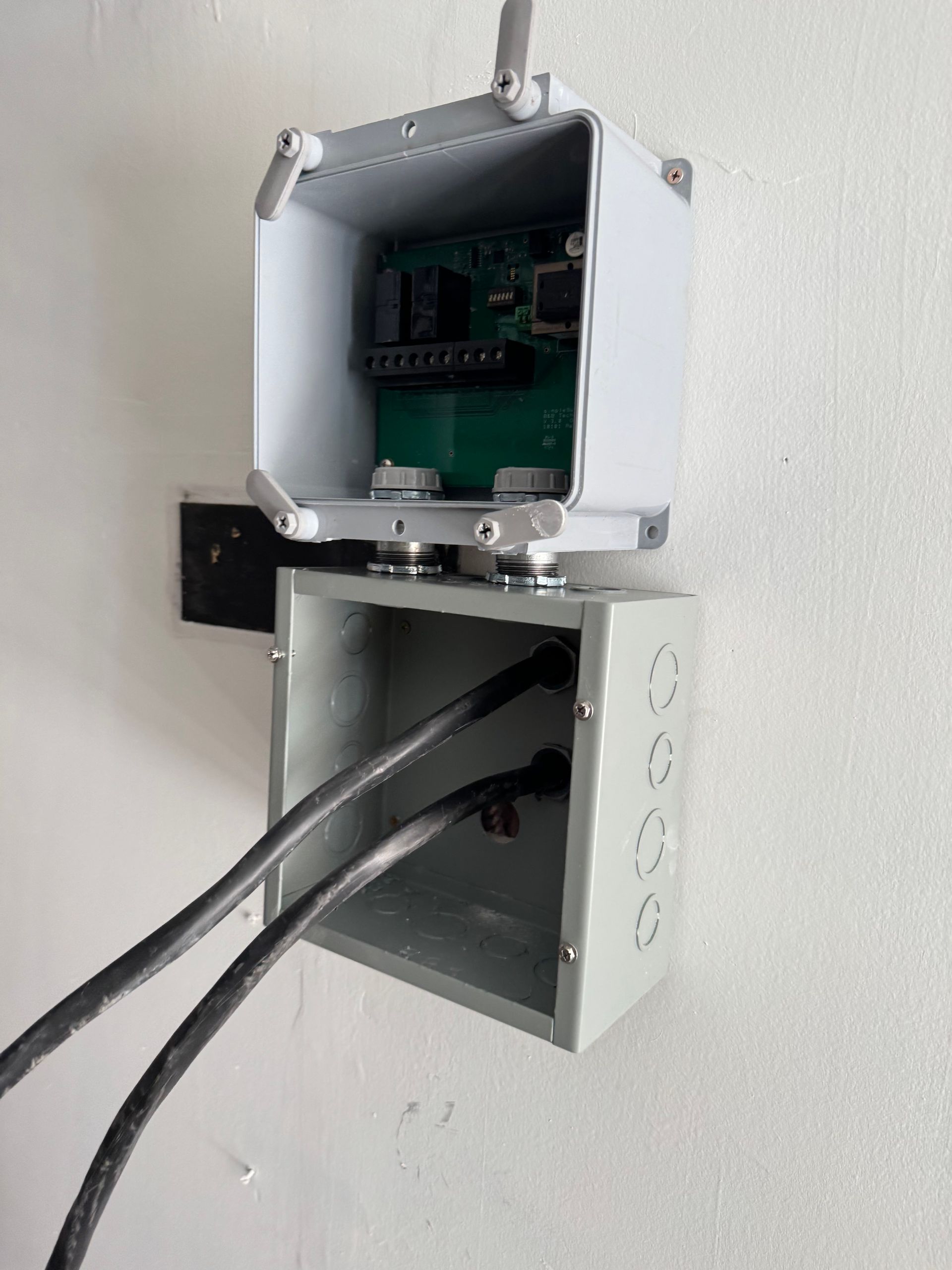 Two stacked electrical junction boxes mounted on a white wall, with exposed wiring entering the bottom box.