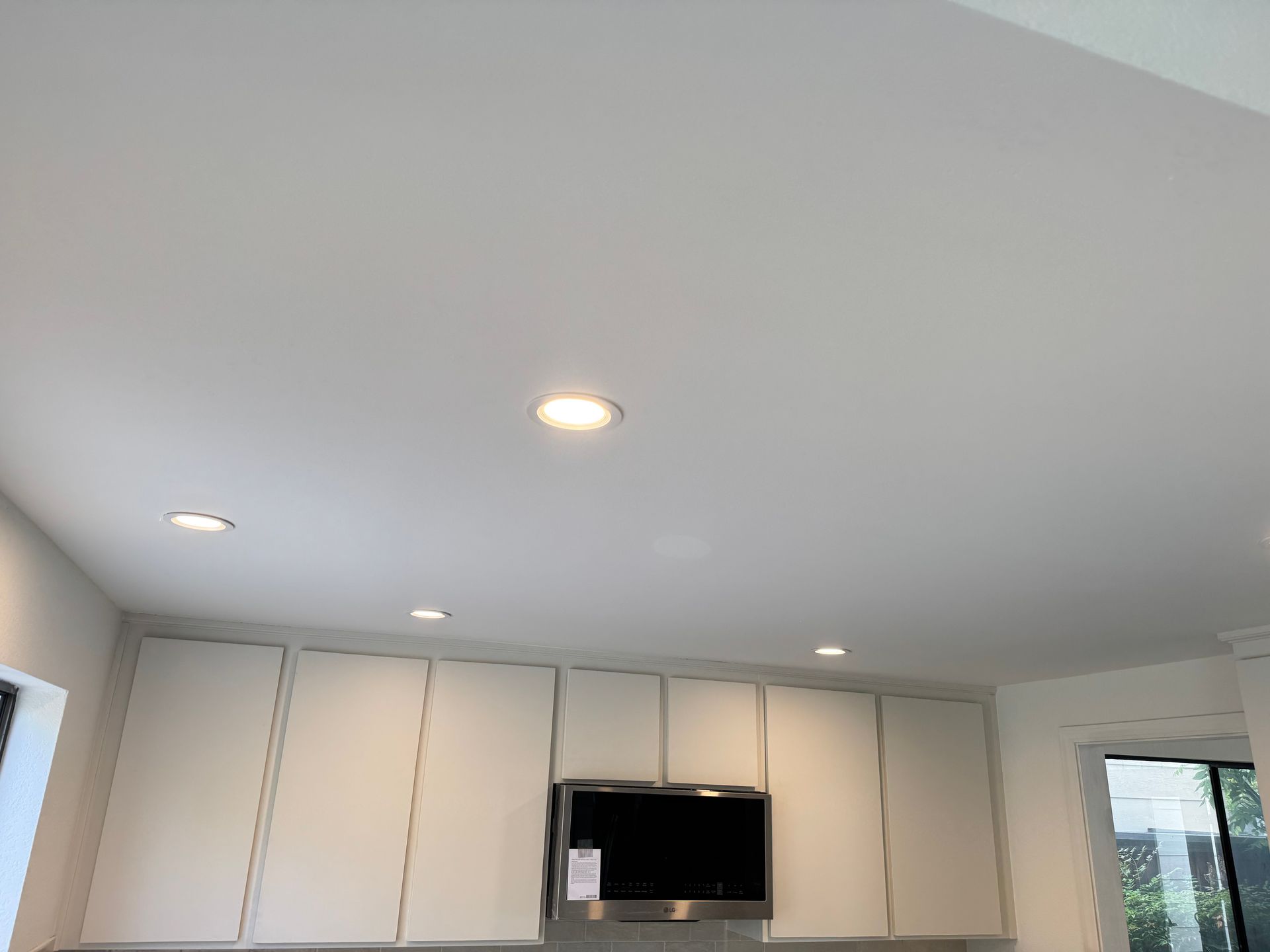 White kitchen cabinets with a stainless steel range hood installed below them and recessed lights in the white ceiling.