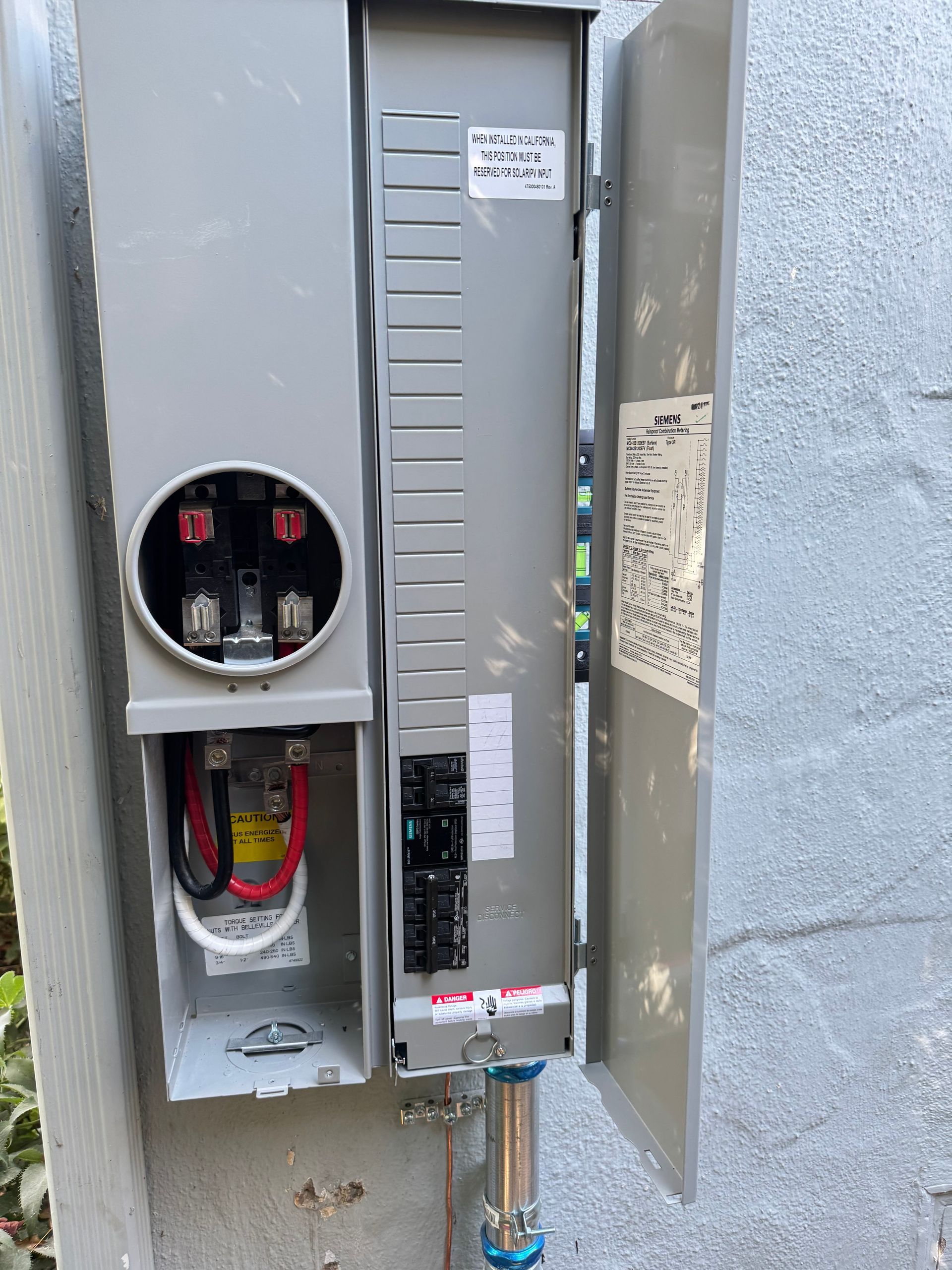 An open outdoor electrical meter socket and service disconnect panel mounted on a textured gray wall.