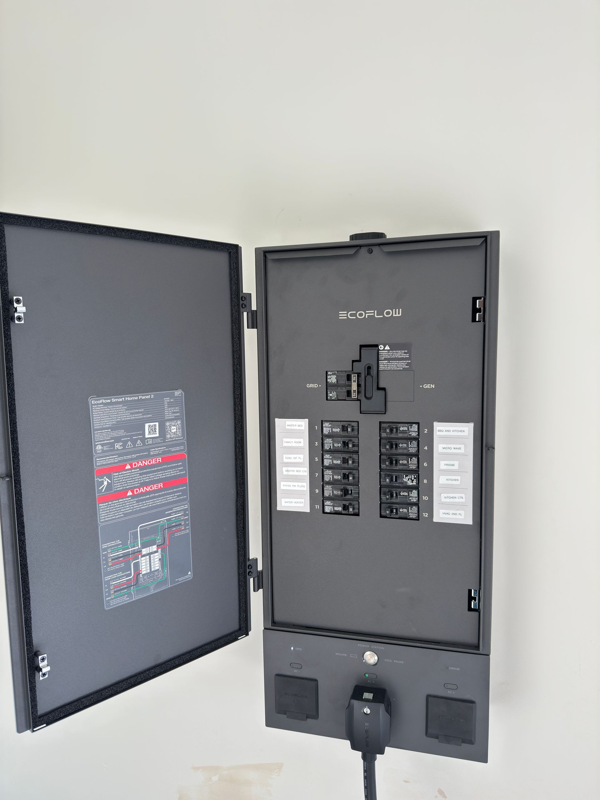 An open grey electrical service panel with a main breaker and multiple branch circuit breakers on a white wall.