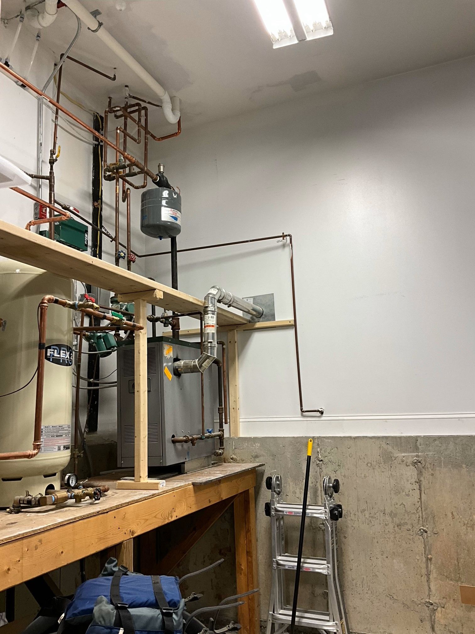 A room with a lot of pipes and a ladder in it.