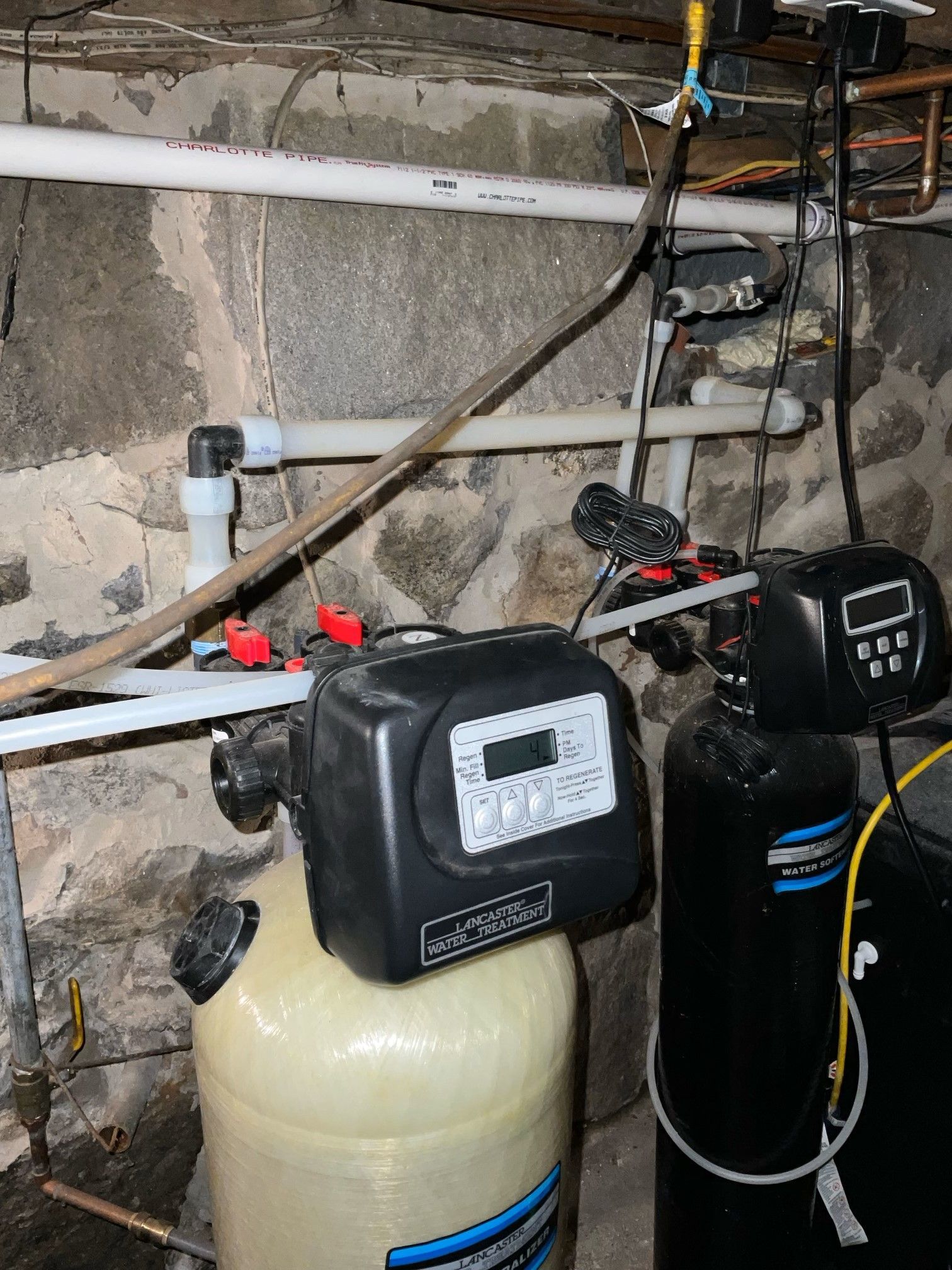 A water treatment system is sitting in a basement next to a stone wall.