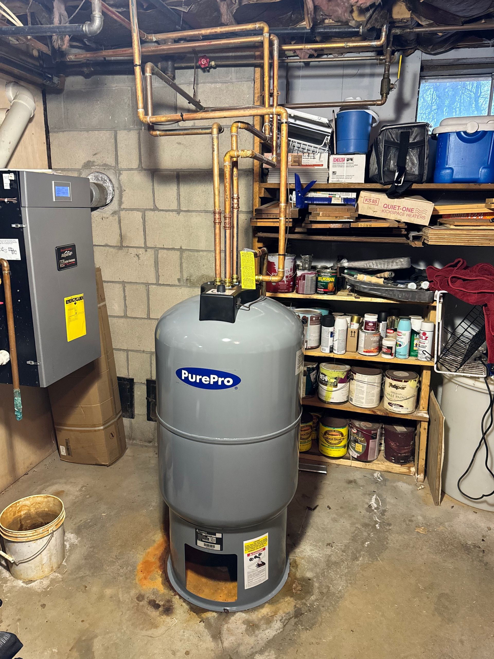 A water heater is sitting in a basement next to a brick wall.