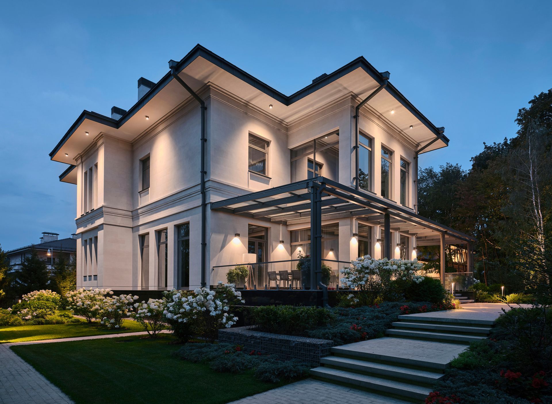 A large white house with a pergola and stairs is lit up at night.