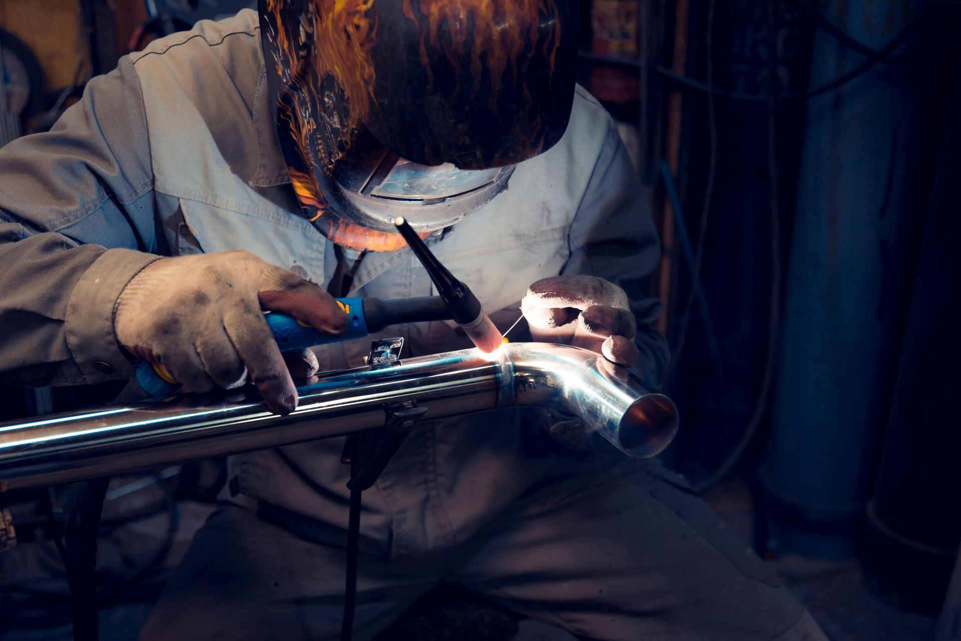 A man is welding a metal pipe in a factory.