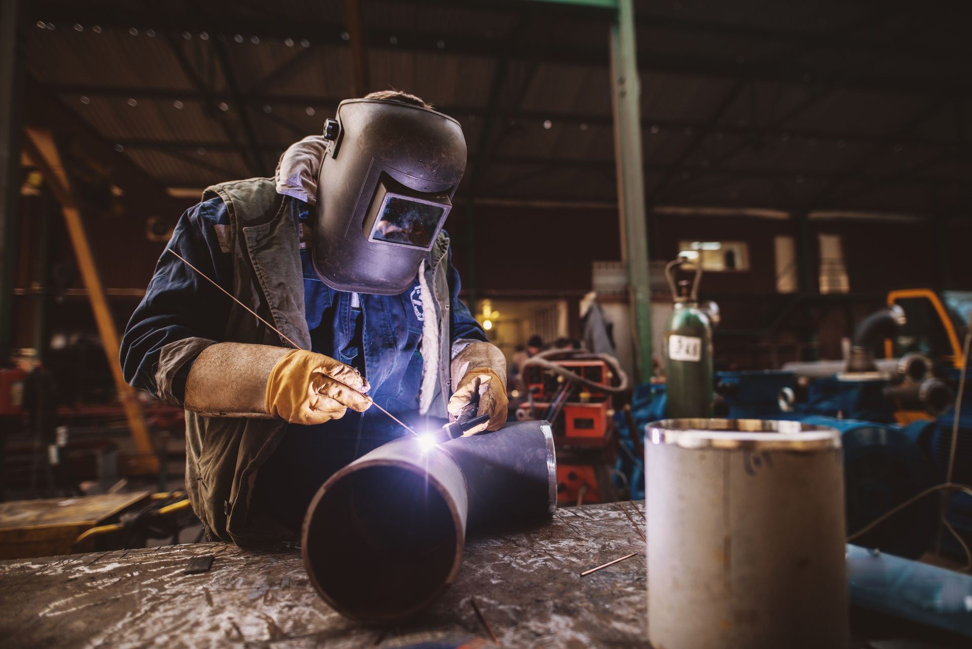 A man is welding a pipe in a factory.