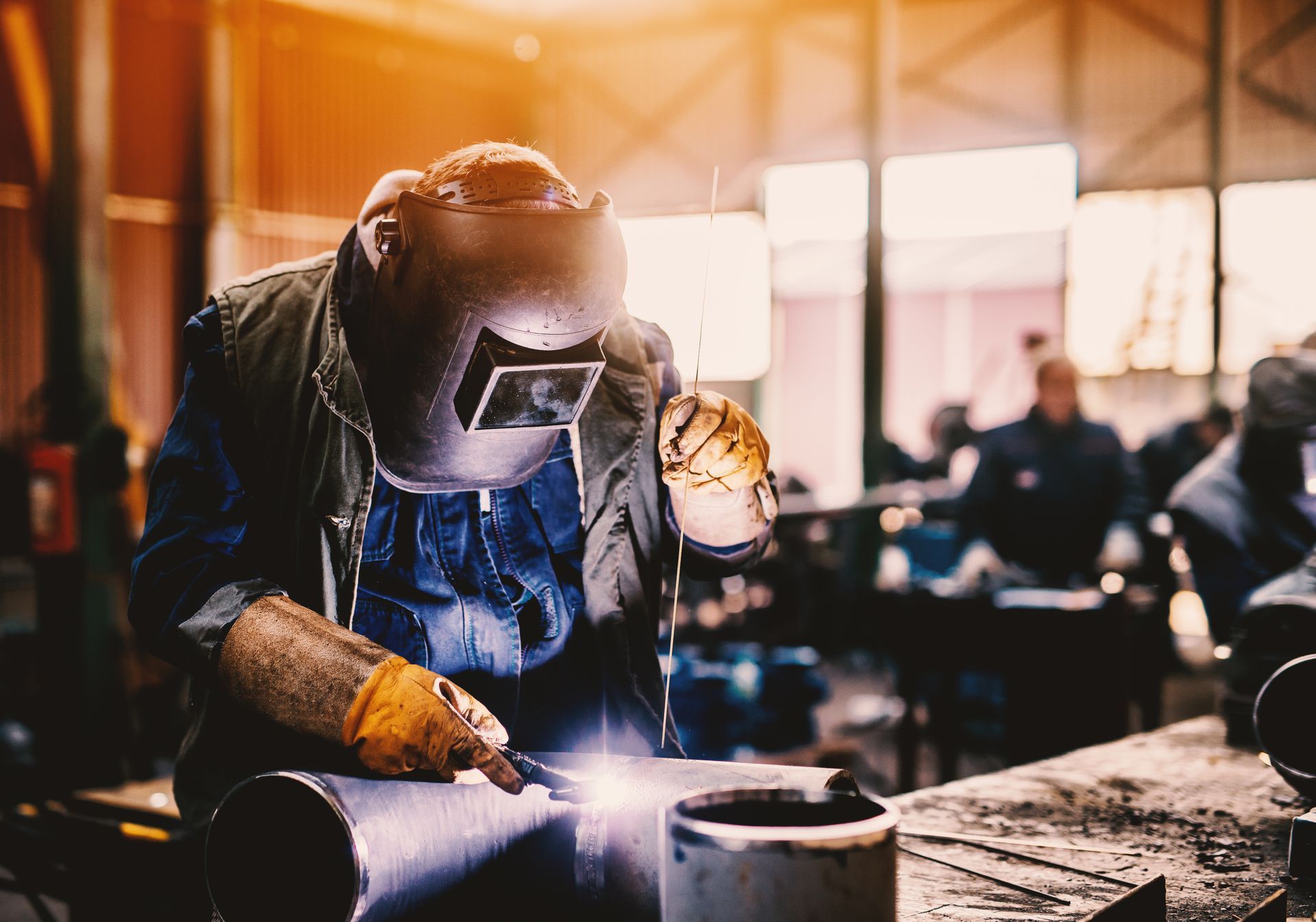 A man wearing a welding mask is welding a pipe in a factory.