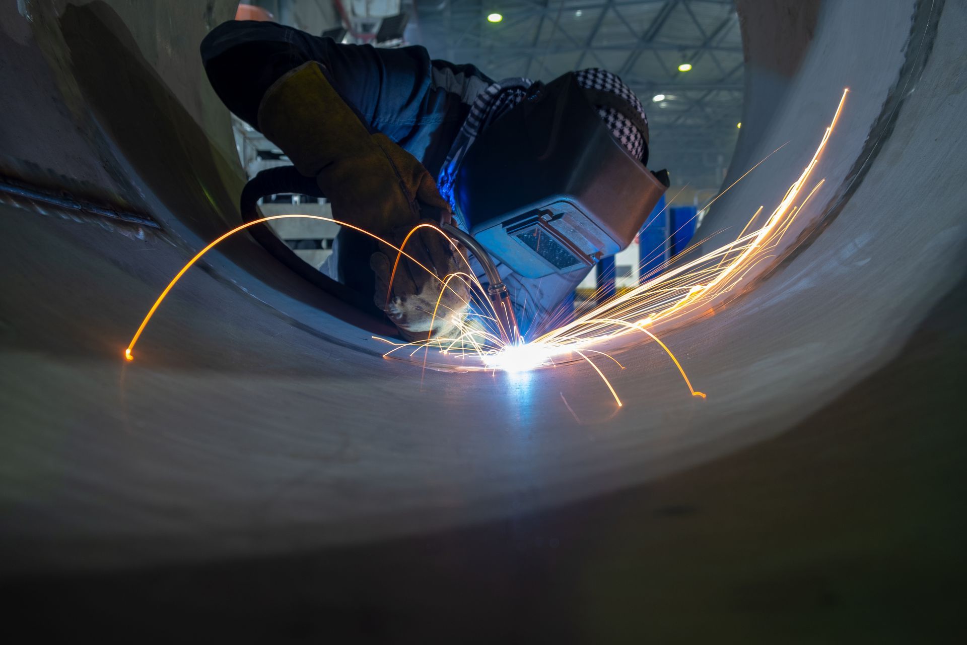 A man is welding a pipe in a factory.