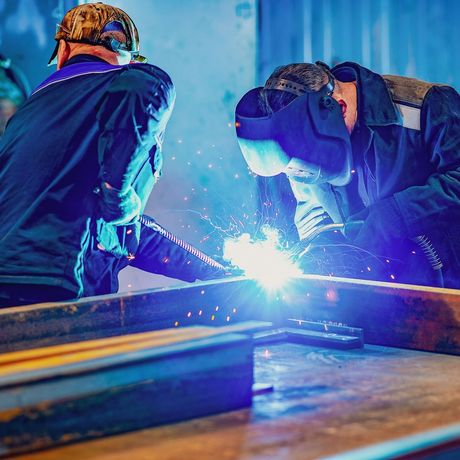 Two men are welding a piece of metal in a factory.