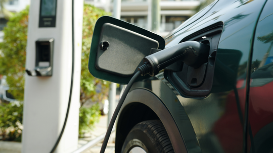 Green electric car charging at a station with the charging cable plugged in.