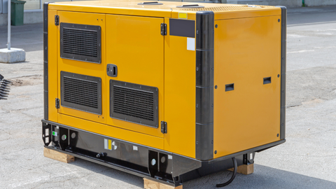 Yellow industrial generator on a wooden pallet, set on pavement.