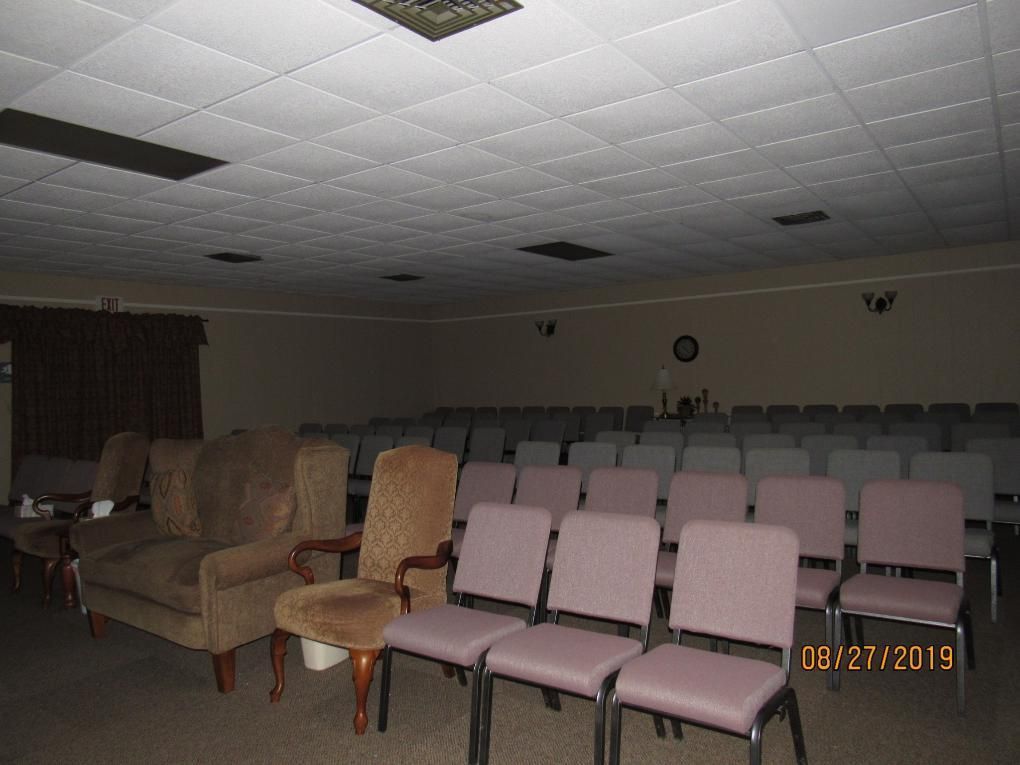 Empty room with rows of chairs, a few armchairs, and a dark ceiling with lights.
