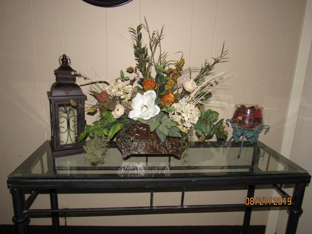 Floral arrangement with lantern and candle holder on a glass-topped table.